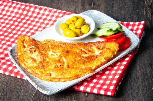 Free Golden omelette served with green olives, cucumbers, and tomatoes on a checkered cloth. Stock Photo