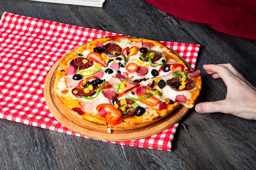 A person is holding a pizza on a checkered tablecloth
