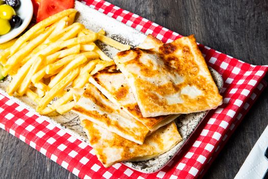 Tasty grilled quesadillas with crispy fries and colorful olives on a rustic plate.