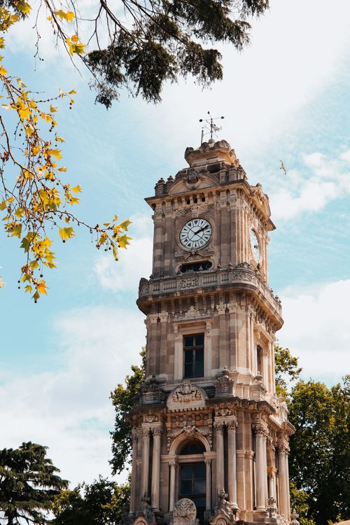Free The iconic Dolmabahçe Clock Tower in Istanbul, Turkey, framed by leafy branches on a bright day. Stock Photo