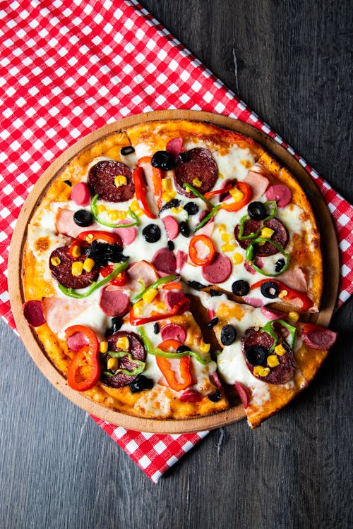 A pizza with meat, cheese and vegetables on a red checkered tablecloth