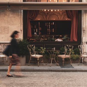 A stylish woman walks past an inviting European bistro, with elegant seating outside.
