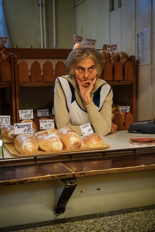 Free Elderly woman tending a bakery in Breslau, Poland, surrounded by fresh bread and price tags. Stock Photo
