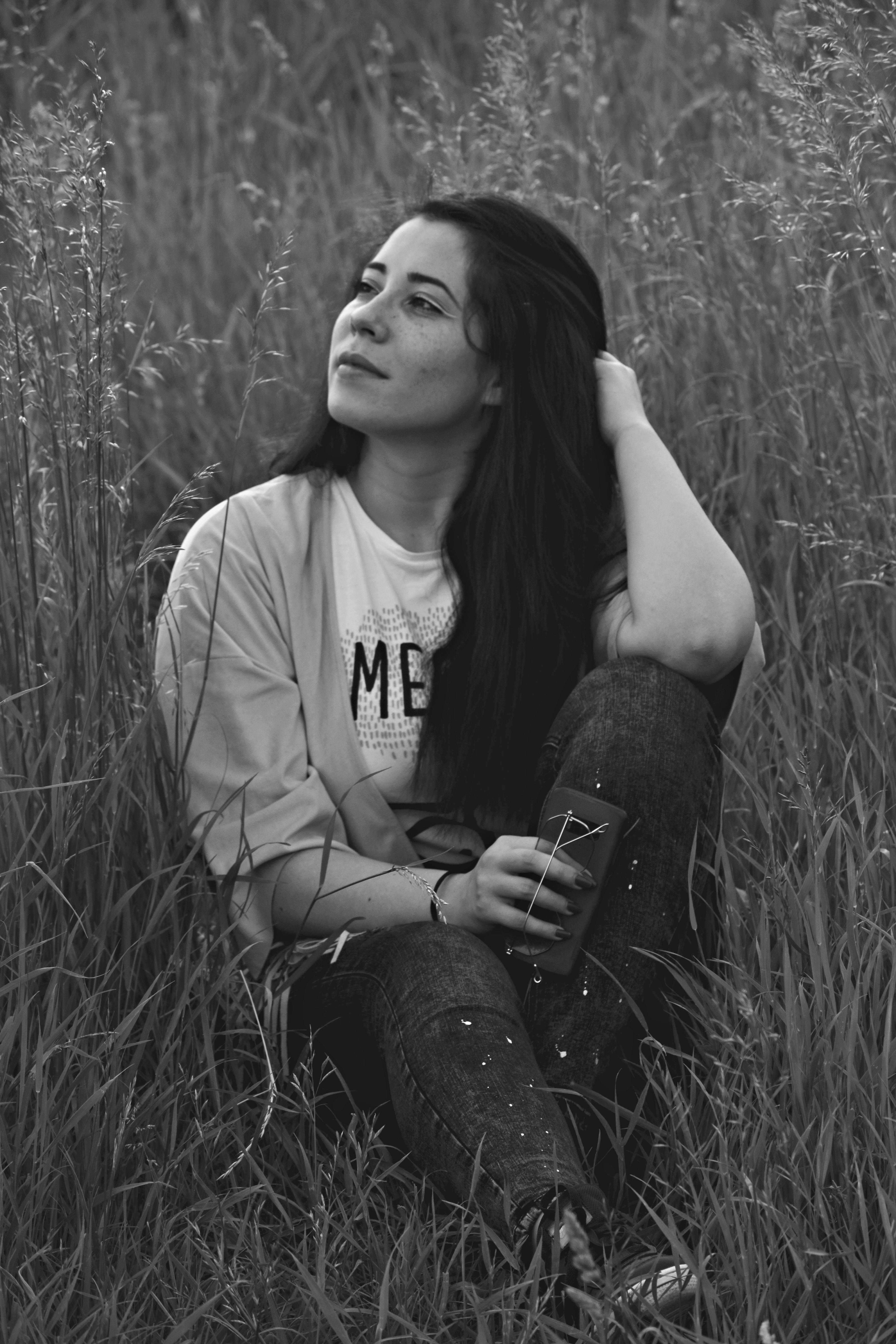 一名女子坐在草地上，手持智能手机的黑白肖像