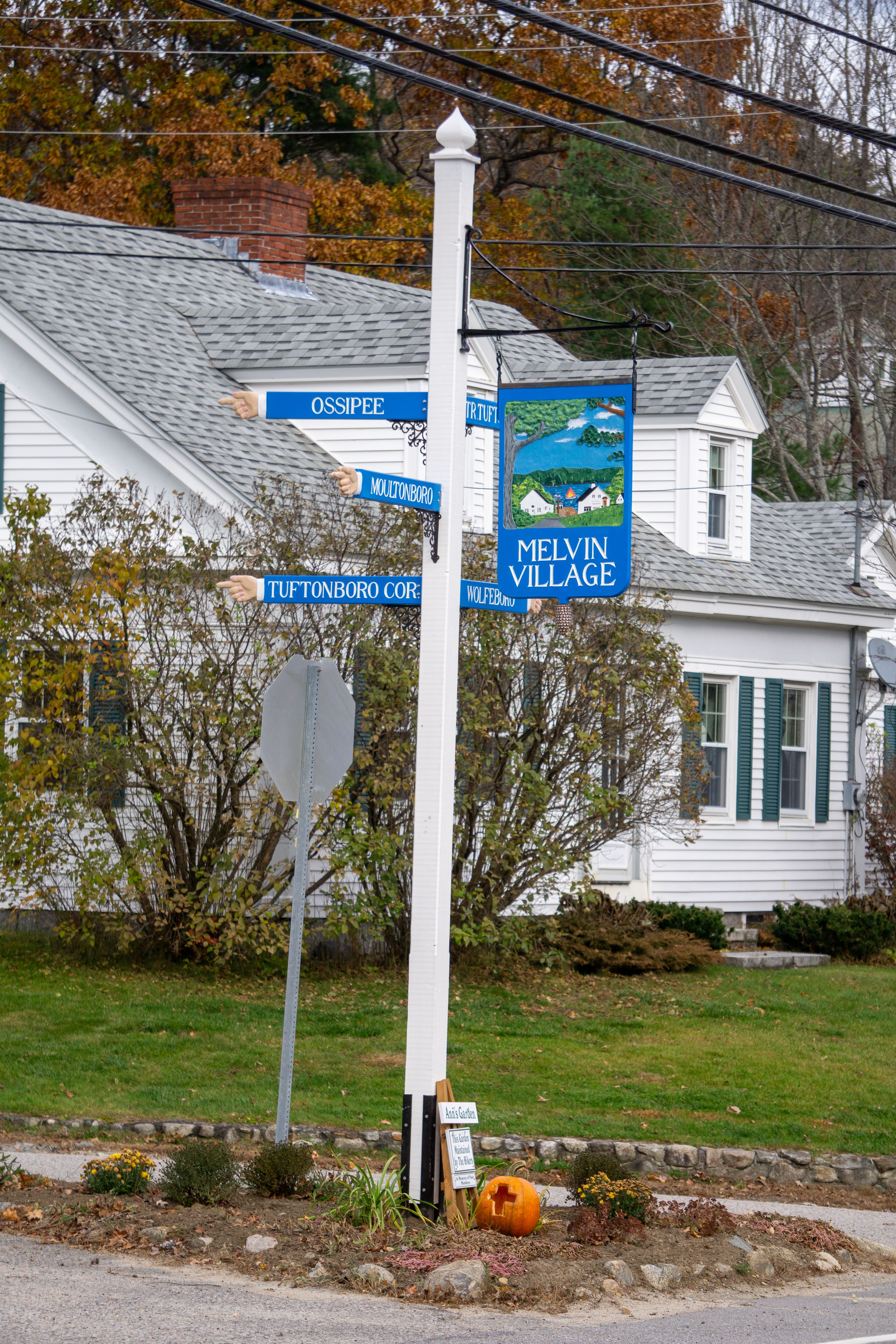 Charming street sign in Melvin Village with colorful autumn trees and a cozy house.