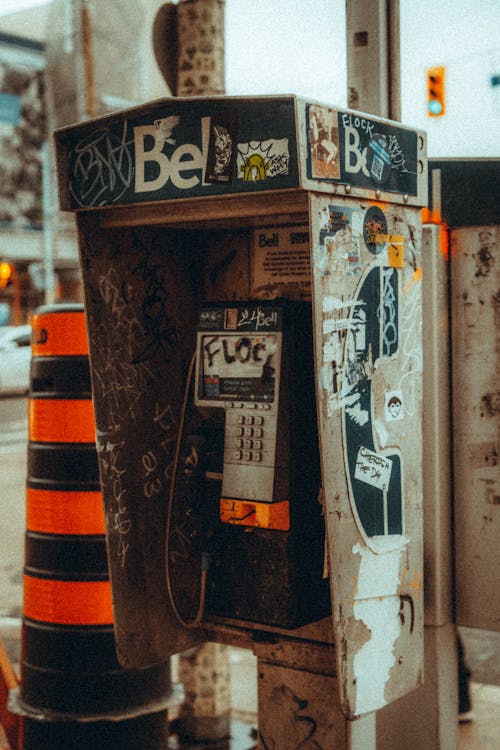 A pay phone with graffiti on it sitting on a street corner