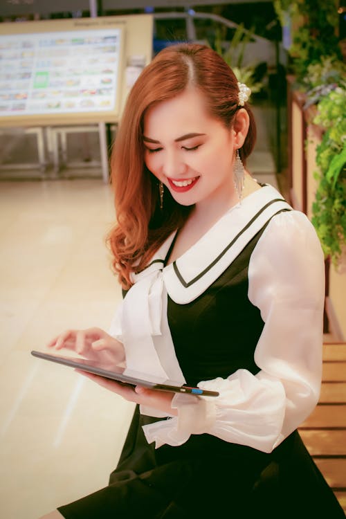 태블릿을 사용하는 동안 서있는 흑백 복장에 웃는 여자의 사진