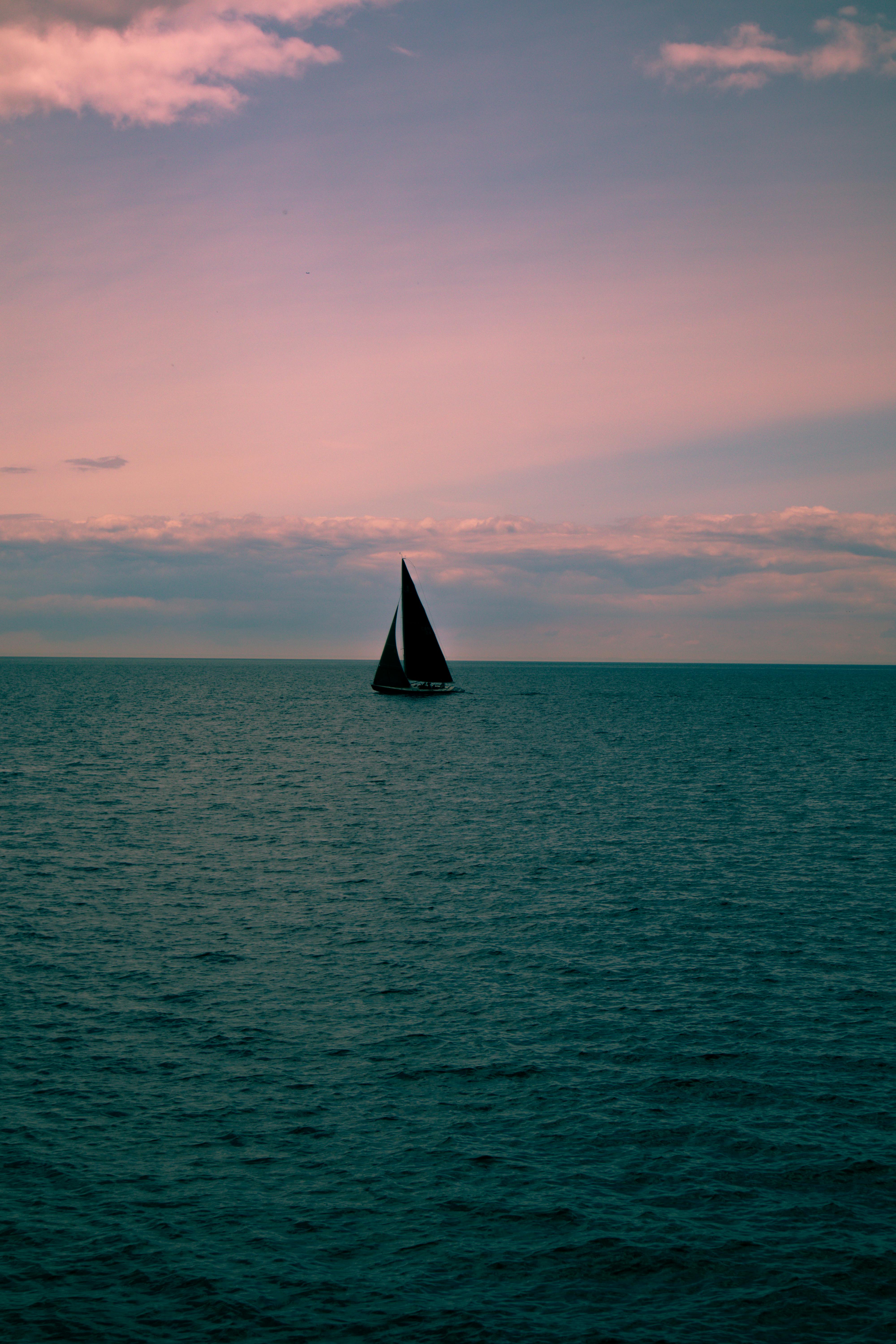 A solitary sailboat silhouette glides across the calm sea during a colorful dusk.