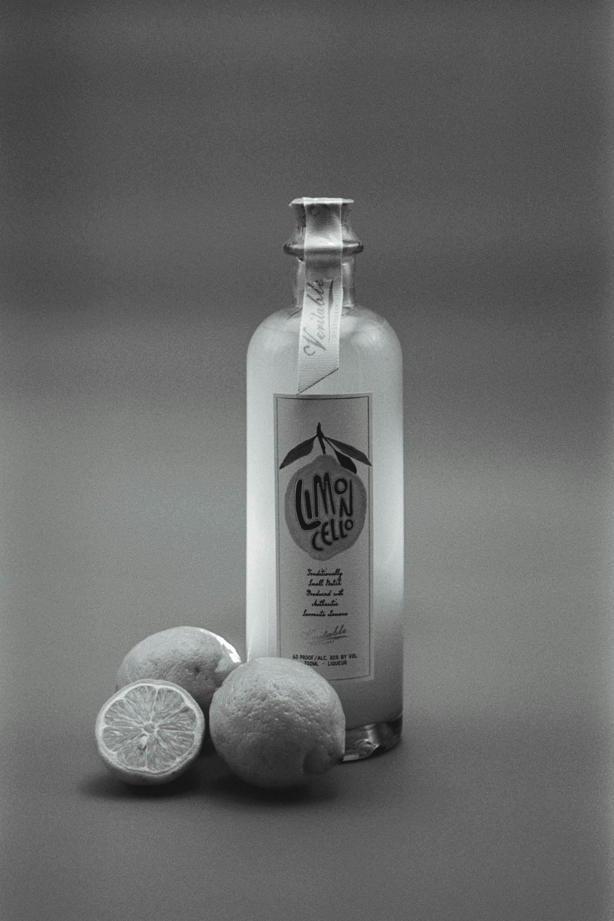 Elegant black and white still life of a limoncello bottle with fresh lemons in a studio setting.