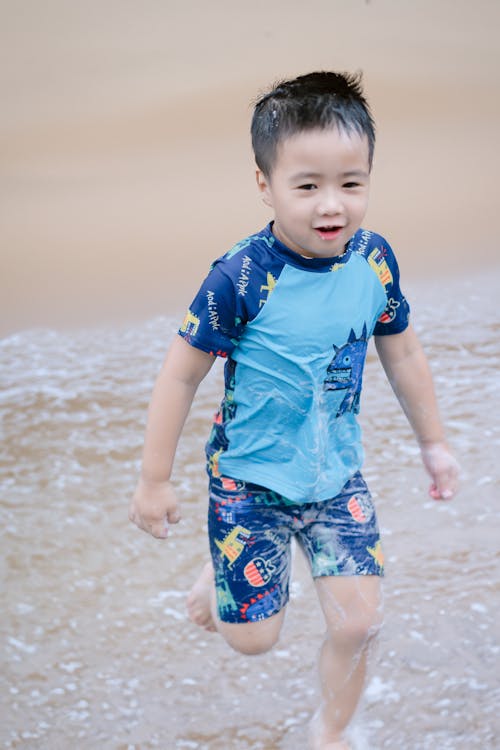 A young boy running through the water in a blue shirt