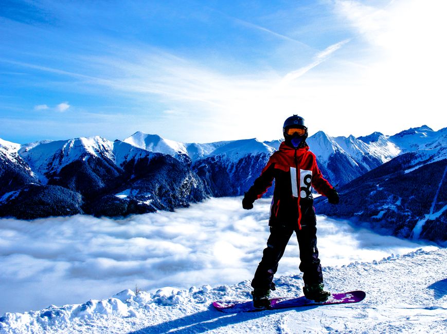 A focused Canadian snowboarder standing at the top of a snowy mountain peak in winter