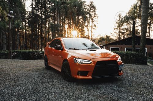 Free An orange sports car parked on gravel with a scenic rural background at sunset, capturing natural beauty. Stock Photo