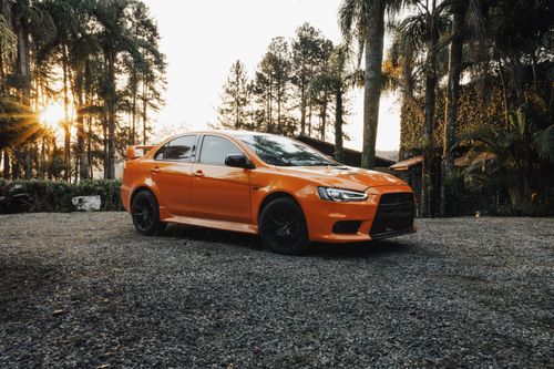 Free Orange sports car parked on gravel driveway at sunset amidst lush trees. Stock Photo
