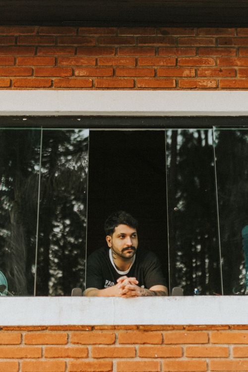 Free Man with mustache leaning on window sill of brick building, looking outside. Stock Photo
