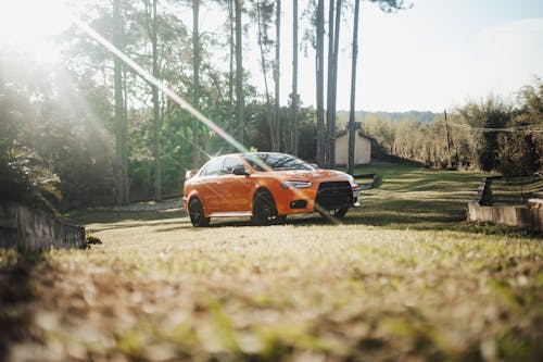 An orange car parked in the grass near trees