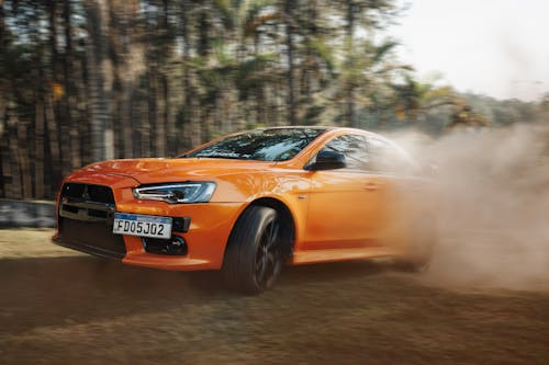 The orange car is driving through the dirt