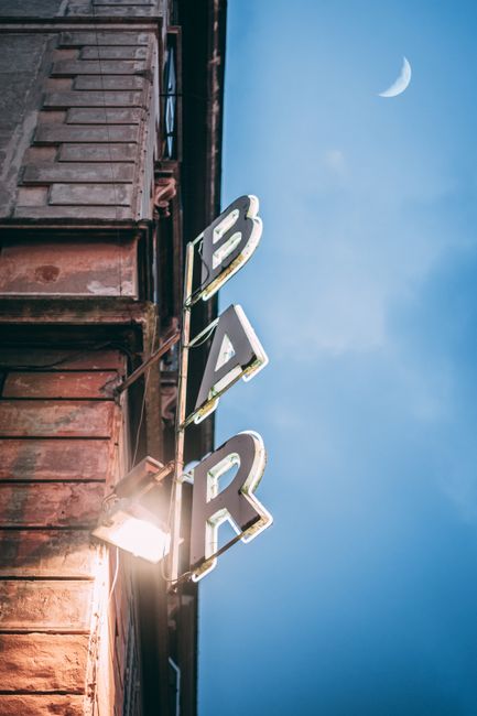 Illuminated bar sign on a building facade in Rome with a crescent moon in the evening sky.