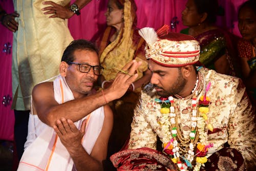 A man in traditional attire is putting his finger on the forehead of another man
