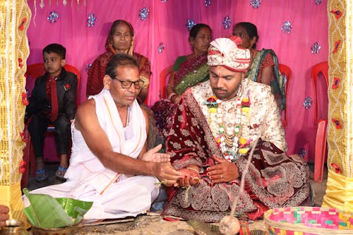 A man in traditional attire is giving a woman a ring