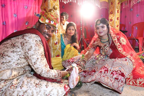 A bride and groom in traditional attire sitting on the ground