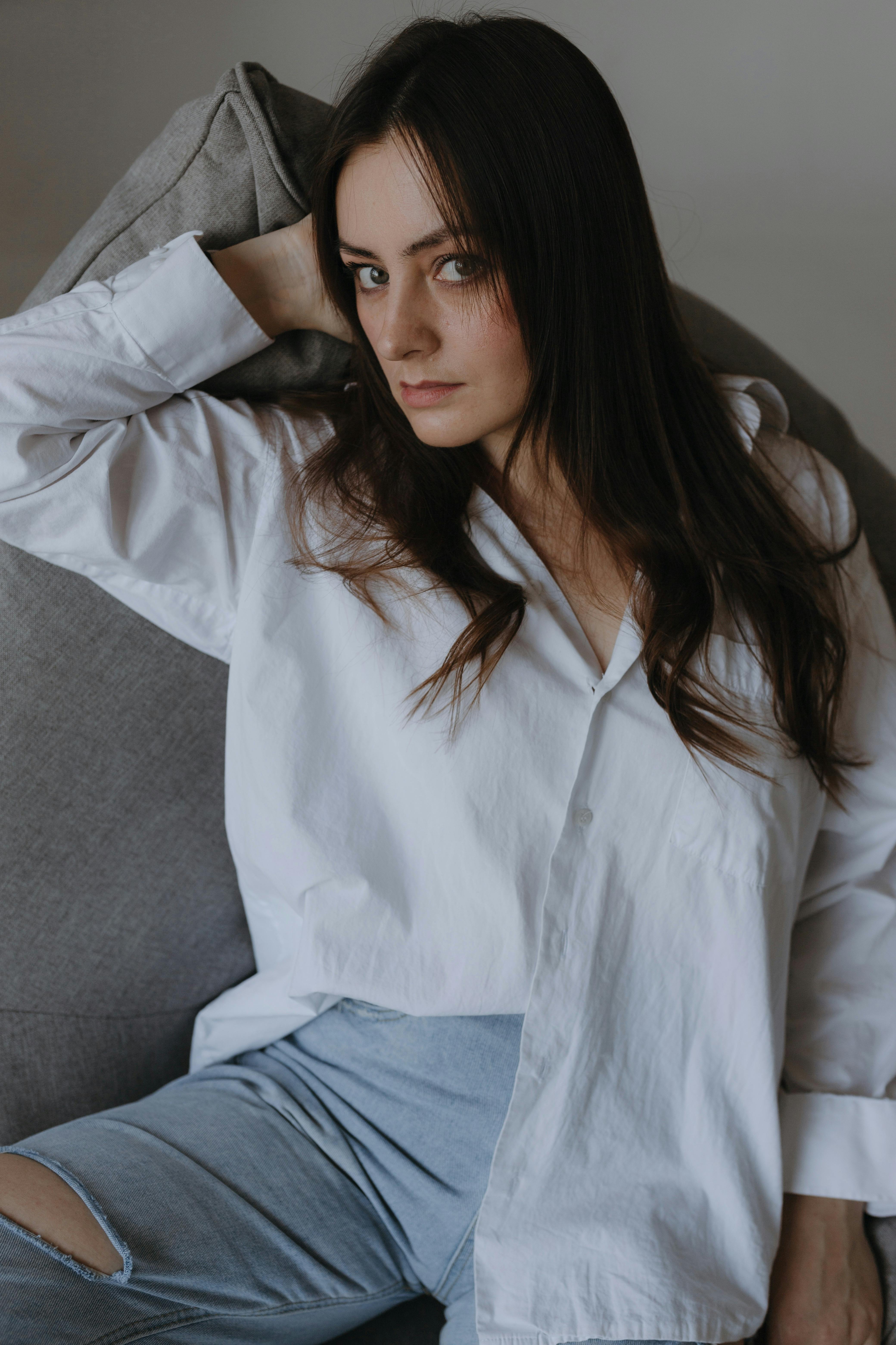 Portrait of a young brunette woman in a white shirt and jeans posing indoors.