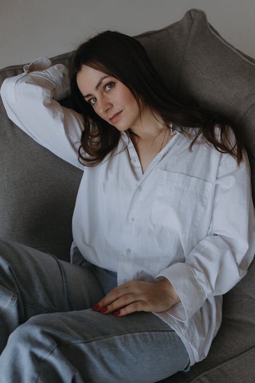 A woman in white shirt and jeans sitting on a couch