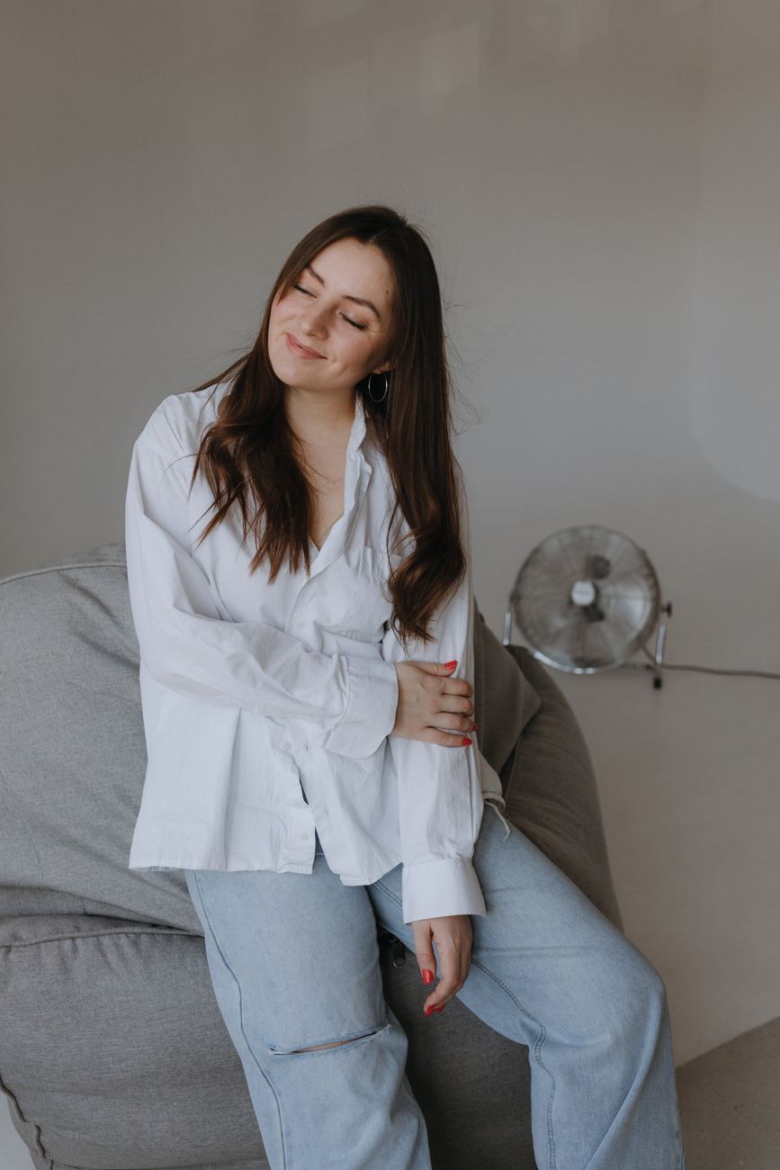 Portrait of a smiling young woman in casual attire, seated indoors with a soft backdrop.