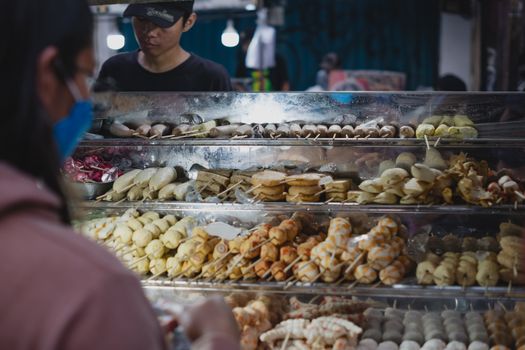Assorted skewers displayed at an outdoor street food market with a vendor and customer.