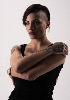 Studio shot of a stylish woman with tattoos and striking hairstyle, showcasing confident fashion.