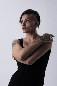 A striking portrait of a tattooed woman in a black dress in a studio setting.