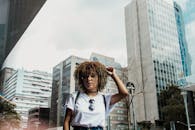 一位卷发戴太阳镜的女人在现代都市的高楼景观中摆姿势