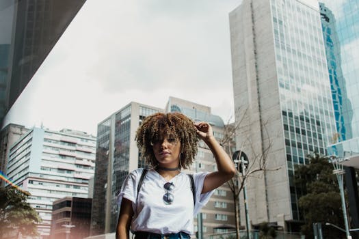 一位卷发戴太阳镜的女人在现代都市的高楼景观中摆姿势