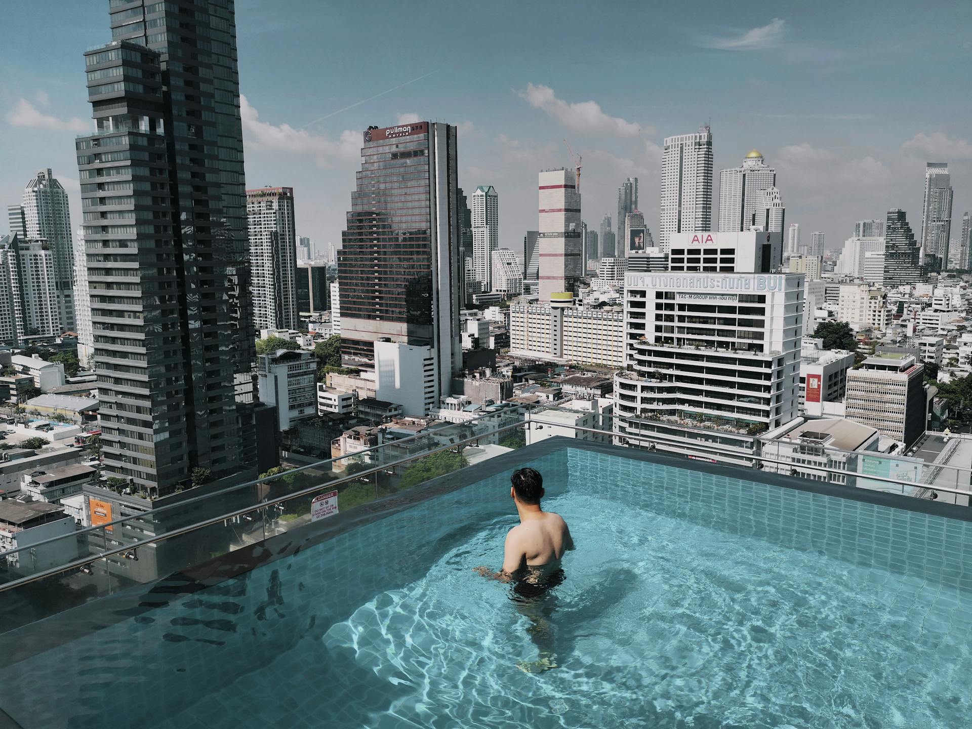 Man in rooftop pool with stunning view of Bangkok skyscrapers, Thailand.