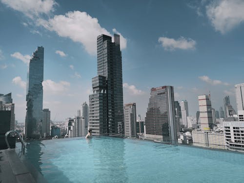 Free Unrecognizable male traveler swimming in rooftop pool on sunny day against futuristic skyscrapers in modern city Stock Photo