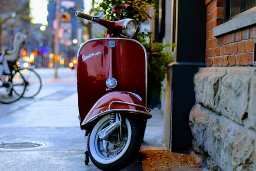 红色piaggio Vespa小型摩托车停在灰色和红色的混凝土建筑旁边