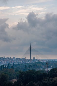 Dramatic skyline view of Ada Bridge in Belgrade, with overcast clouds creating a moody urban landscape.