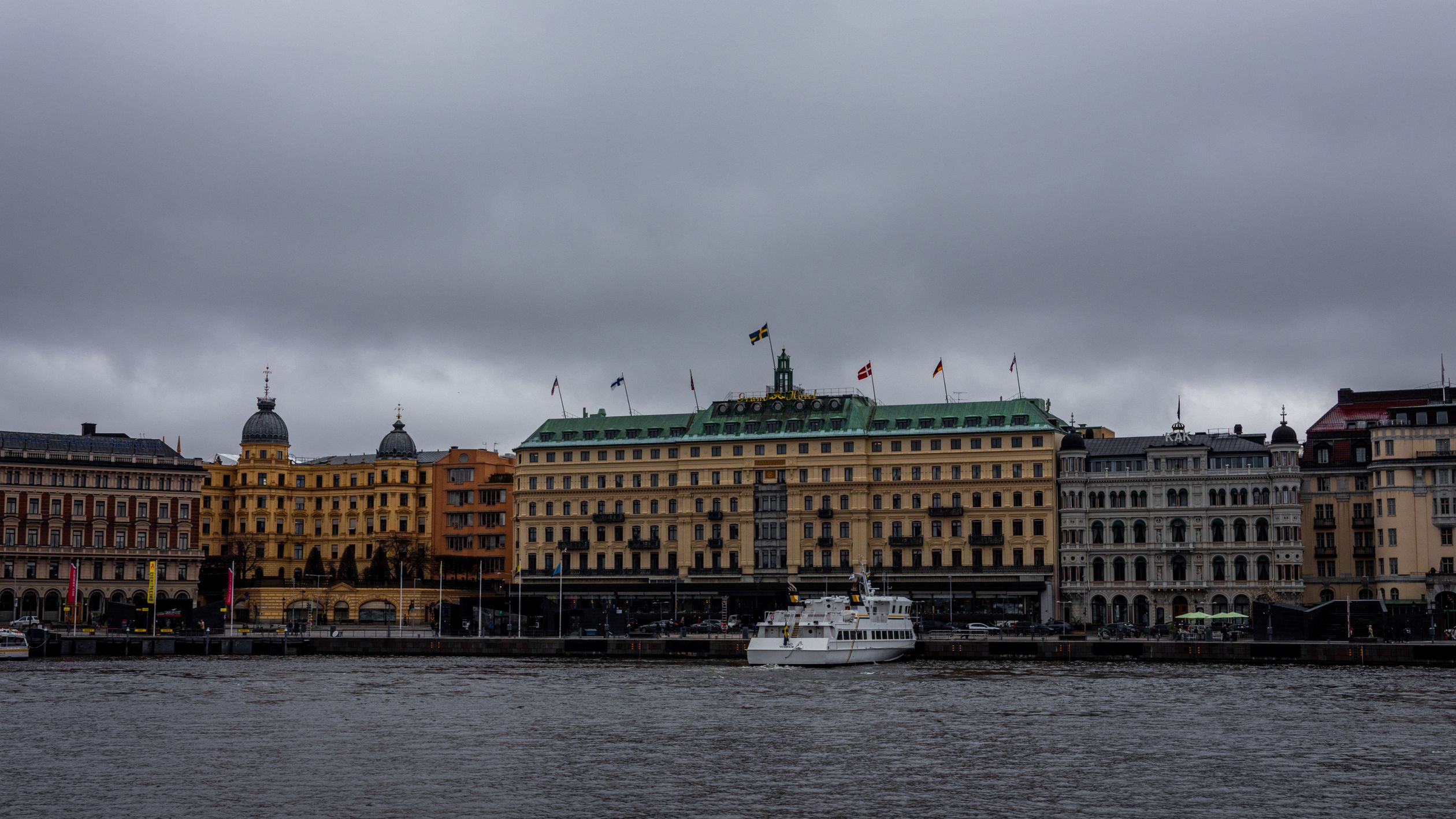 Majestic view of the Grand Hotel and surrounding architecture along Stockholm's waterfront on a cloudy day.