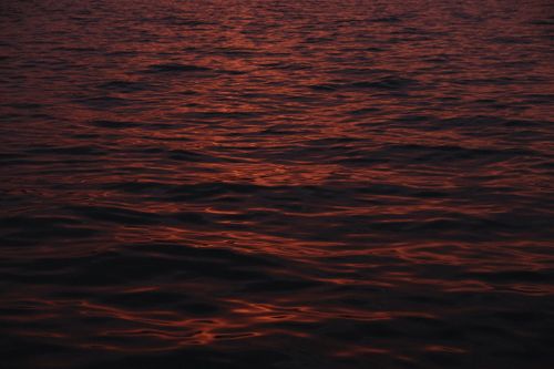 Free Calm ocean waves illuminated by the warm glow of the sunset, creating a peaceful scene. Stock Photo