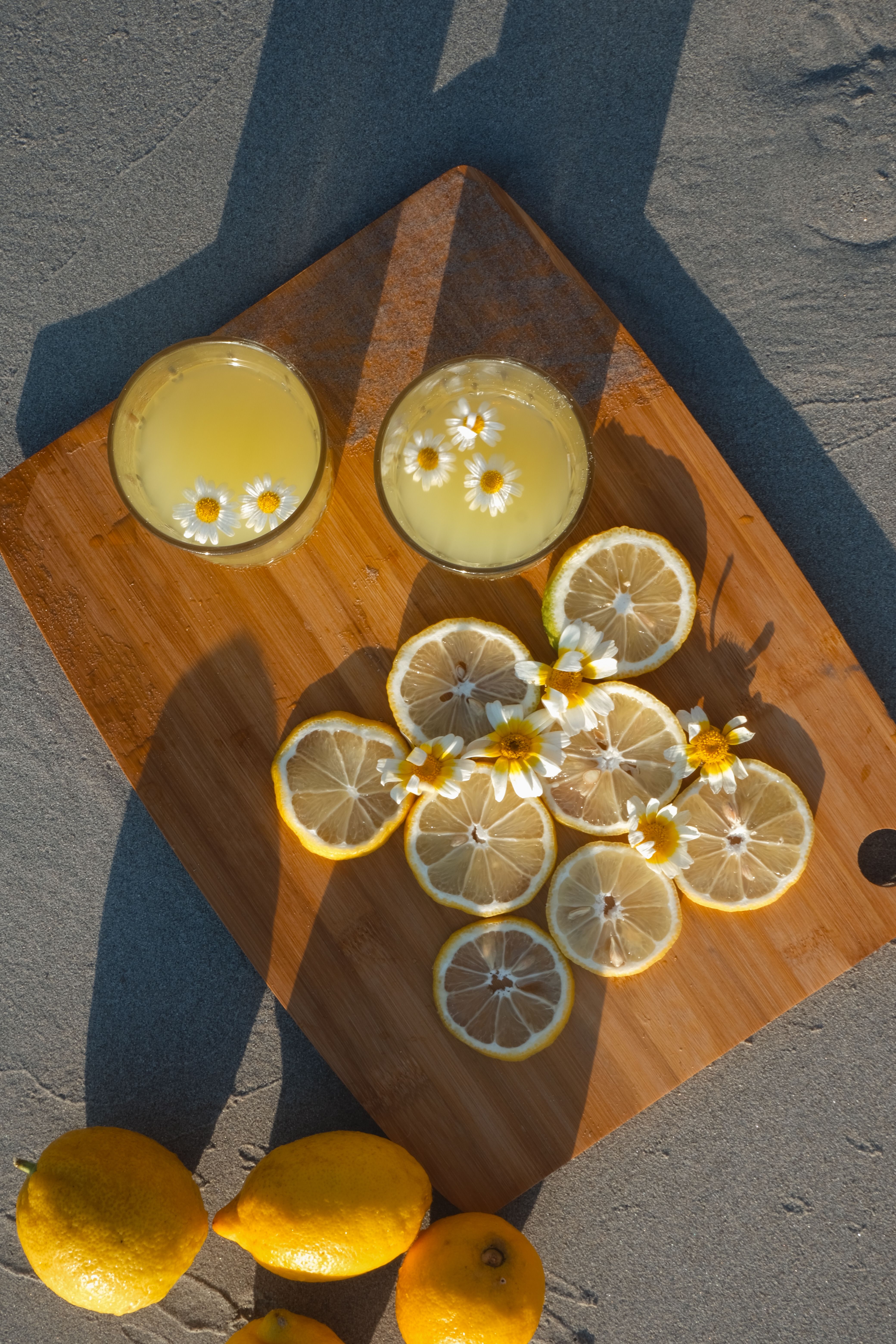 Top view of glasses with lemonade, lemon slices, and flowers on a wooden tray.