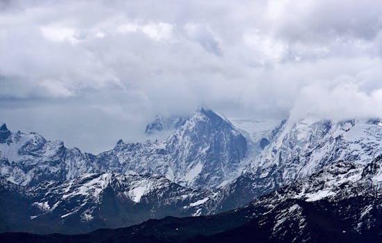 A breathtaking view of a snowcapped mountain range under overcast skies, showcasing nature's raw beauty.