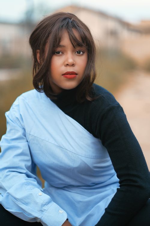 Free Portrait of a fashionable woman sitting outdoors in a blue shirt with a soft focus background. Stock Photo