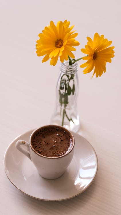 A cup of coffee and a flower on a table