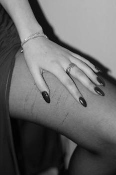 Black and white photo of a woman's hand with jewelry resting on her leg, highlighting elegance.