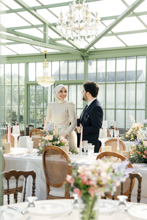 A bride and groom are standing in a glass greenhouse