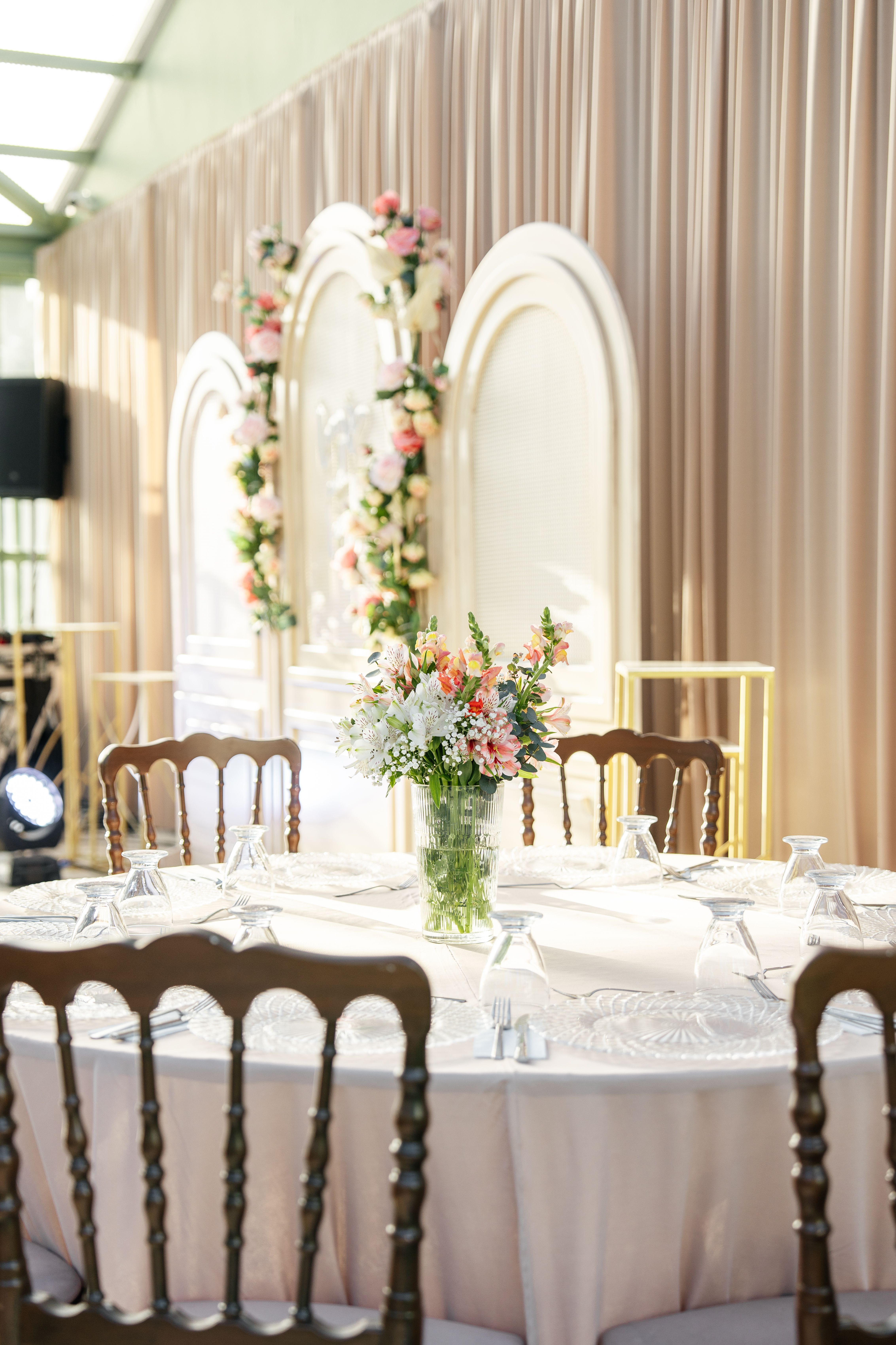 Elegant round table setup for a wedding with floral centerpiece and decorative background arches.