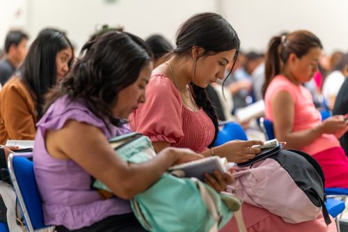 Free Women attentively reading during a gathering in Ciudad de México. Introspective and focused moment. Stock Photo