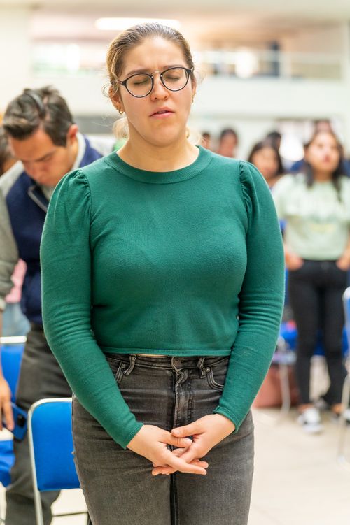 Free Portrait of a woman with eyeglasses praying at an indoor religious gathering. Stock Photo