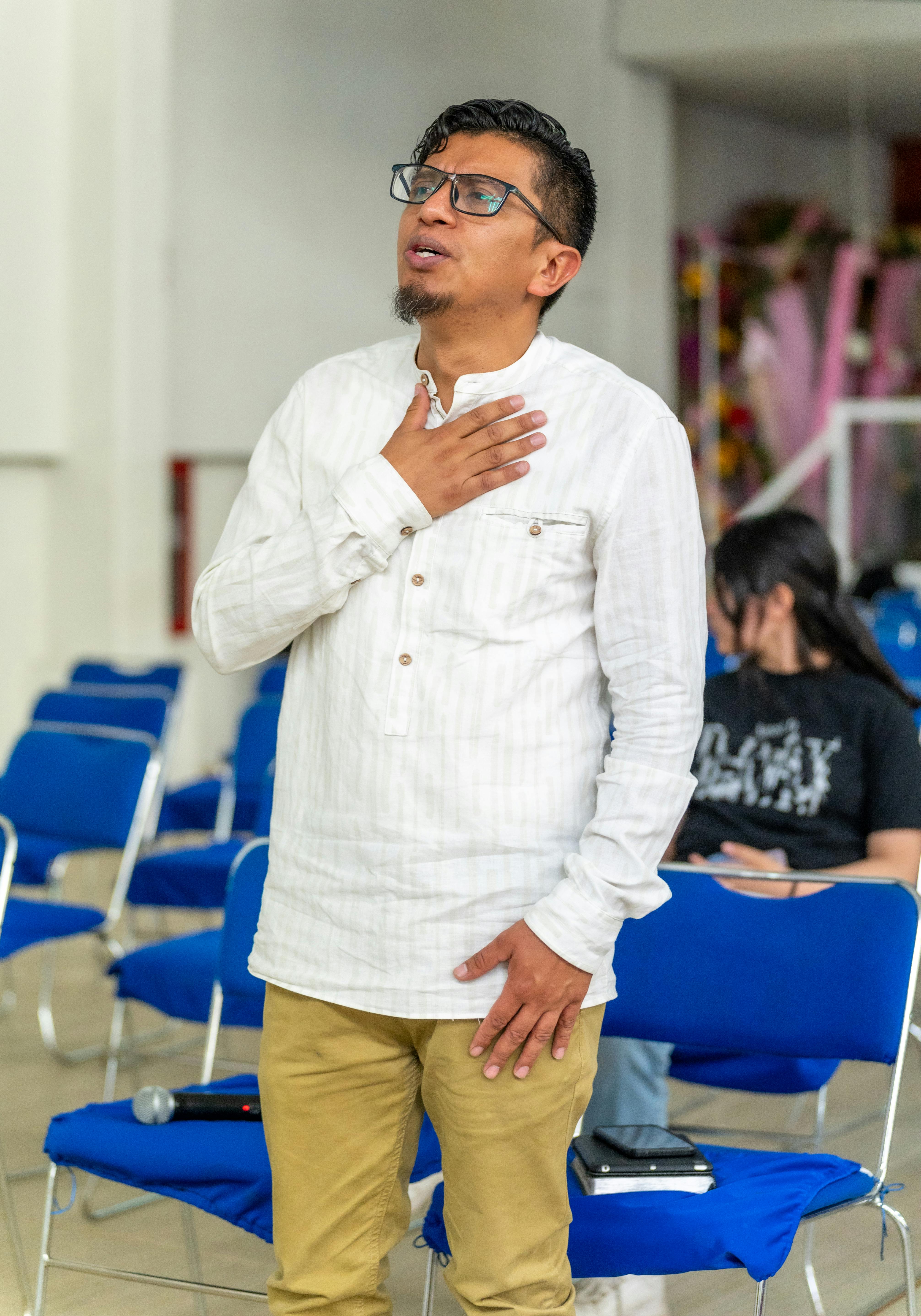Young man in white shirt praying with hand on heart in a church setting, CDMX.