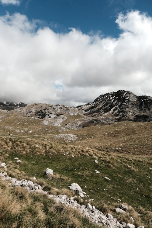 A mountain range with grass and rocks under a cloudy sky