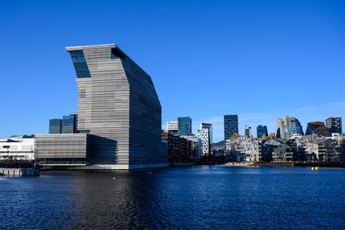Stunning view of the contemporary Munch Museum and Oslo skyline reflected on the waterfront under a clear blue sky.